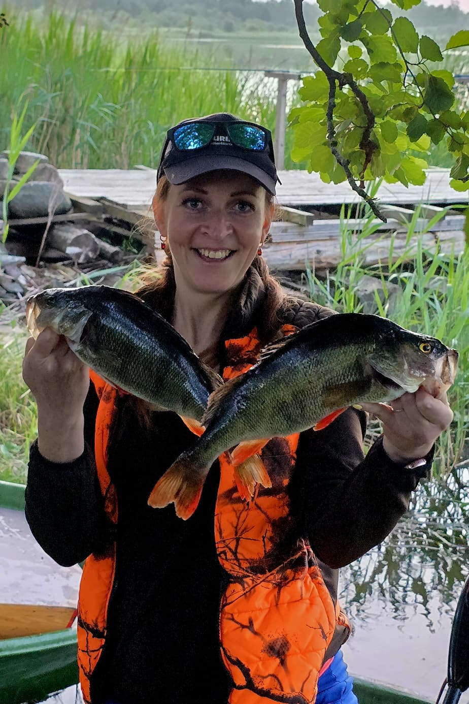 Elīna smiling with two freshly caught perch on a Latvian lake shore