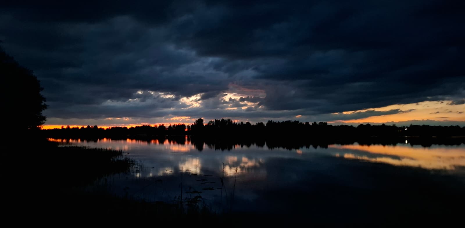Sunset over a calm Latvian lake with dramatic clouds reflecting in the water
